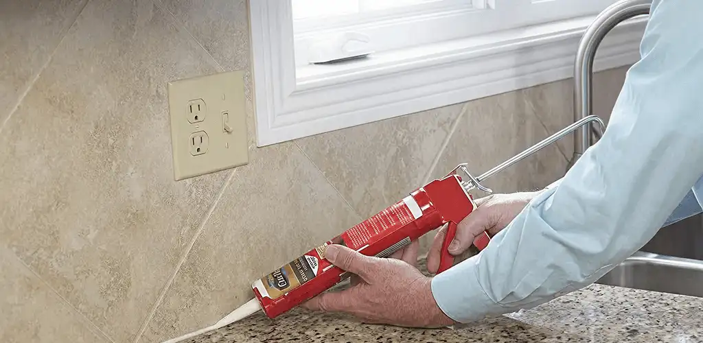Handyman applying caulk along a kitchen backsplash and countertop seam in Columbus, GA