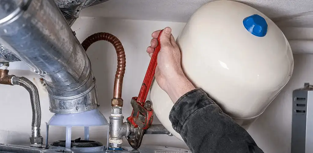 Water heater repair technician tightening plumbing connections near a tank unit in Columbus, GA